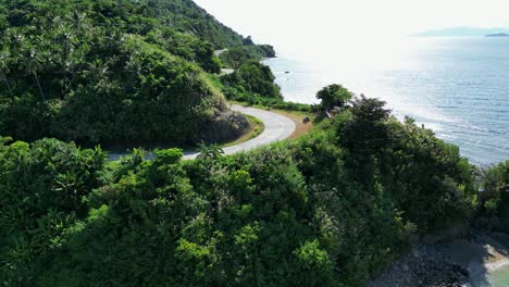 aerial orbit of winding cliffside road on tropical philippine island facing stunning ocean waters