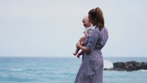 with waves crashing nearby, the mother lifts her son into the air, engaging in playful antics on the sea beach. a joyful young family relishes the moment