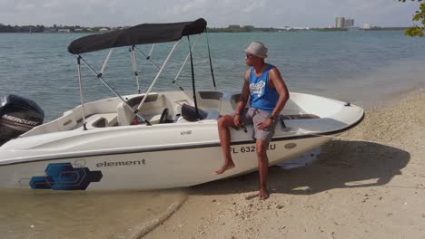 A-model-stands-next-to-his-anchored-boat-at-Morning-Side-island-Miami,-Florida