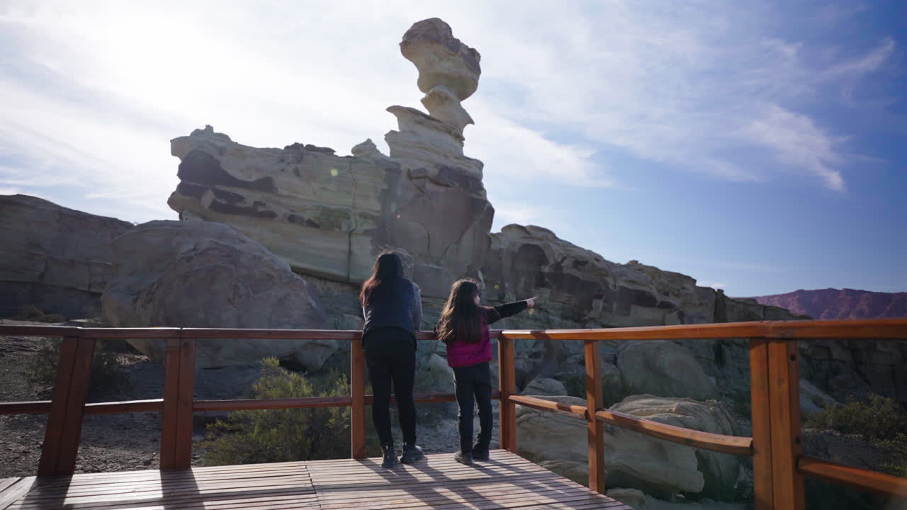 A family observing tall rock formation from wooden Ischigualasto Park Valley of the Moon platform, Argentina