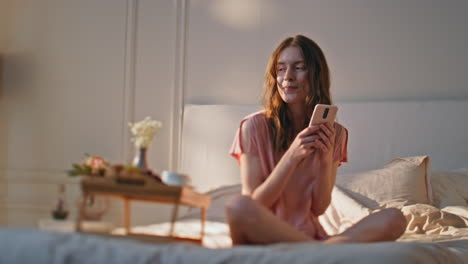 cheerful woman texting smartphone in hotel apartment. dreamy girl enjoy morning