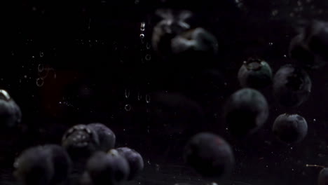 blueberries floating into water on black background