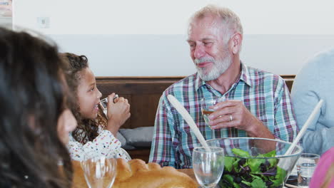 grandfather and granddaughter making a toast as multi-generation family meet for meal at home
