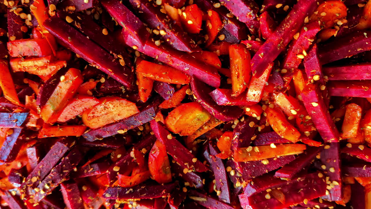Chopped red vegetables of carrots and beets being seasoned for roasting, farm-to-table preparation
