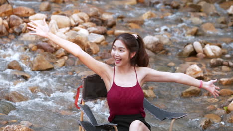 asian woman in red sitting on a chair with big rocks and water slow splashing for relaxing and happiness in the vacation summertime