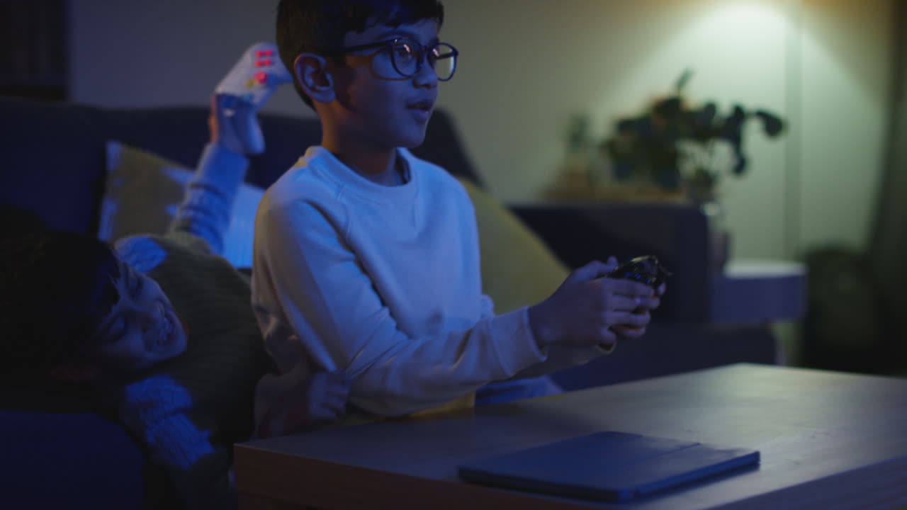 Two Young Boys At Home Having Fun Playing With Computer Games Console On TV Fighting Over Controllers Late At Night 5