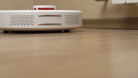 white robotic vacuum cleaner removes debris from the laminate floor view from below