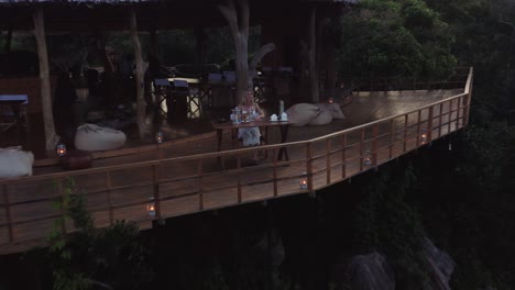 woman enjoys sunset view with glass of wine on wooden safari lodge deck