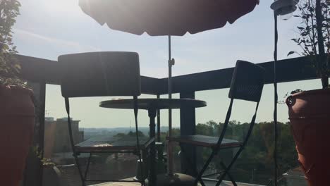 Urban-penthouse-balcony-view-with-vacant-coffee-table-and-two-chairs-under-sun-parasol-swaying-on-breezy-day-in-Belgrade-in-4k