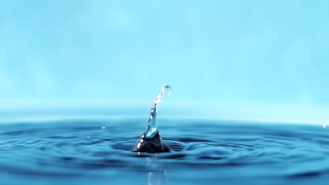 vídeo en 4k en cámara lenta de una superficie de agua con gotas que caen sobre un fondo azul. salpicaduras de agua. rodaje de estudio.