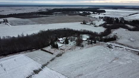 Vista-Aérea-De-Drones-De-Casas-De-Campo-Y-Tierras-De-Cultivo-Cubiertas-De-Una-Capa-De-Nieve-En-Invierno-Oscuro