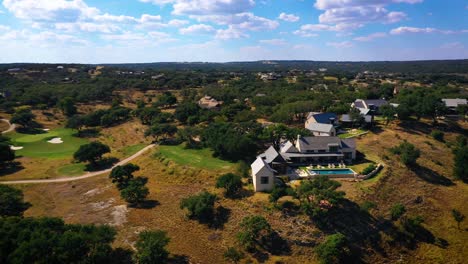 mansion on hill overlooking golf course with swimming pool on sunny day in texas country club aerial fly away blue sky