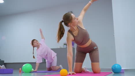 el instructor de gimnasia conduce a los niños en ejercicios de estiramiento de brazos durante una sesión de entrenamiento, con varios equipos de gimnasio y esteras de yoga visibles