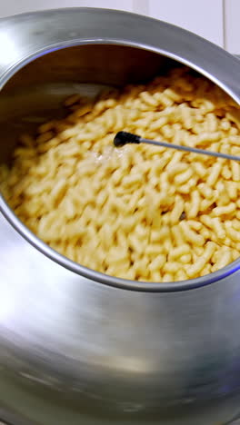 corn snack sticks being sprayed with sweet syrup in the rotating tank. snack production at modern food factory. vertical video