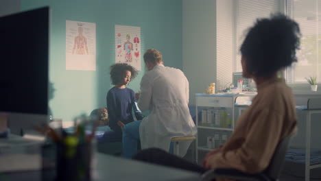 Doctor-measuring-pressure-african-teen-girl-with-stethoscope-in-mother-presence.