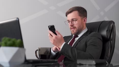 businessman-sitting-in-chair-examining-news-in-smartphone