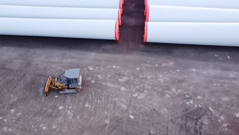 bulldozer estacionado cerca de los enormes componentes de la torre de la turbina eólica en una fábrica de molinos de viento en monroe, michigan - disparo de drones inclinados hacia arriba