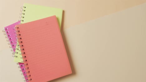 overhead view of colourful notebooks with copy space on beige background, in slow motion