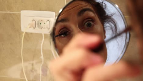 woman painting her eyelash seen from circular mirror