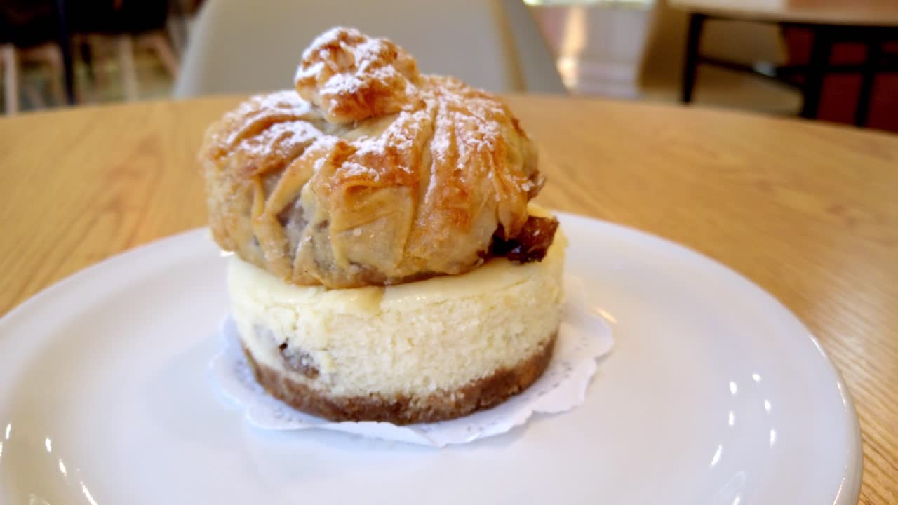 Close-up of layered strudel and cheesecake dessert on white plate over wooden table