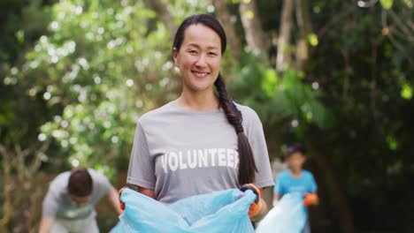 smiling asian woman wearing volunteer t shirt holding refuse sack for collecting plastic waste