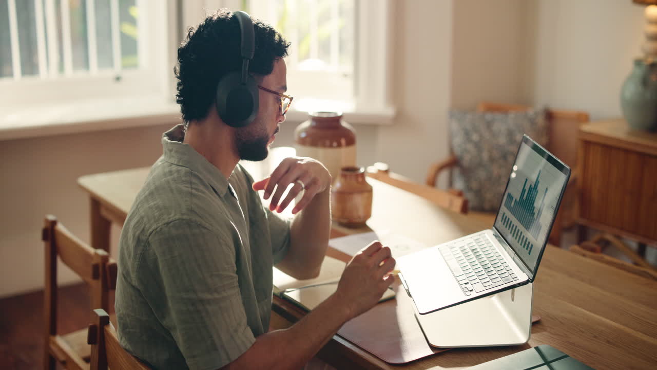 Young Man with Headphones Working on Laptop and Taking Notes at Home