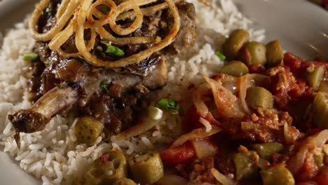 Chuleta-De-Cerdo-Rellena-Sobre-Una-Cama-De-Arroz-Cubierta-Con-Elegantes-Aros-De-Cebolla-Frita-Con-Una-Guarnición-De-Okra-Estofada-Y-Tomate,-Deslizador-De-Cerca-4k