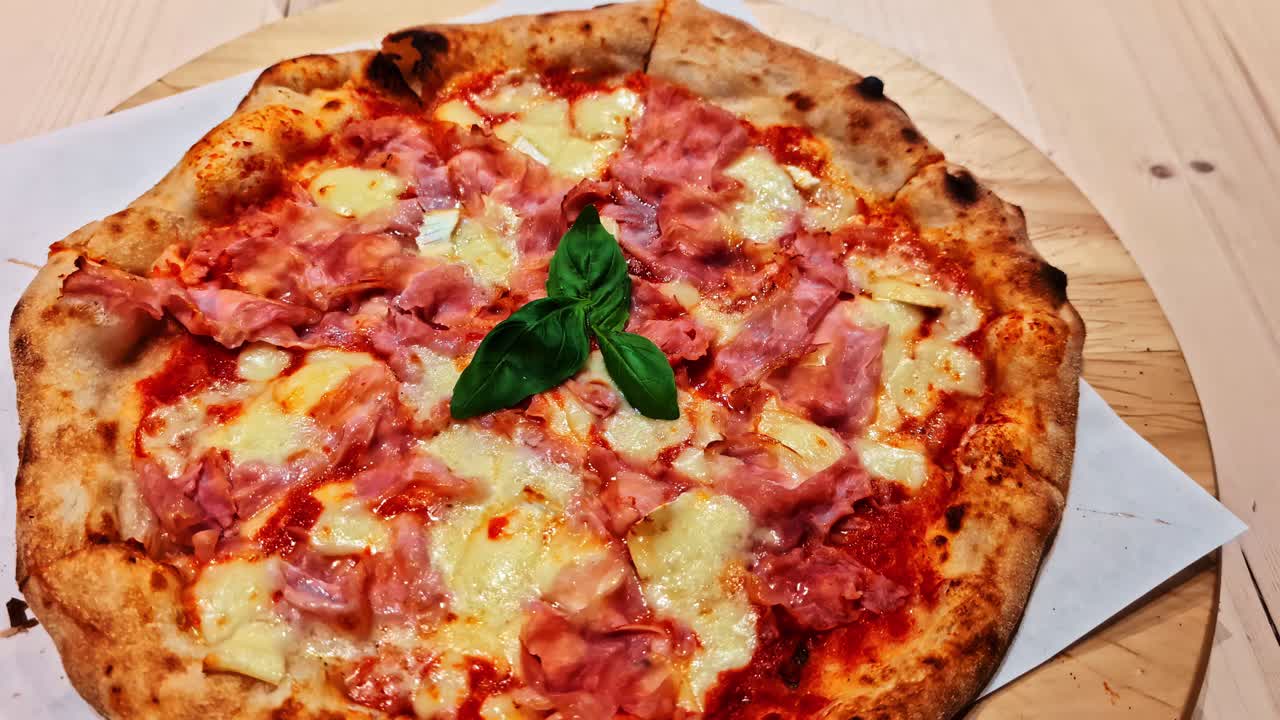 A delicious ham and cheese pizza is finished with a few basil leaves in the middle