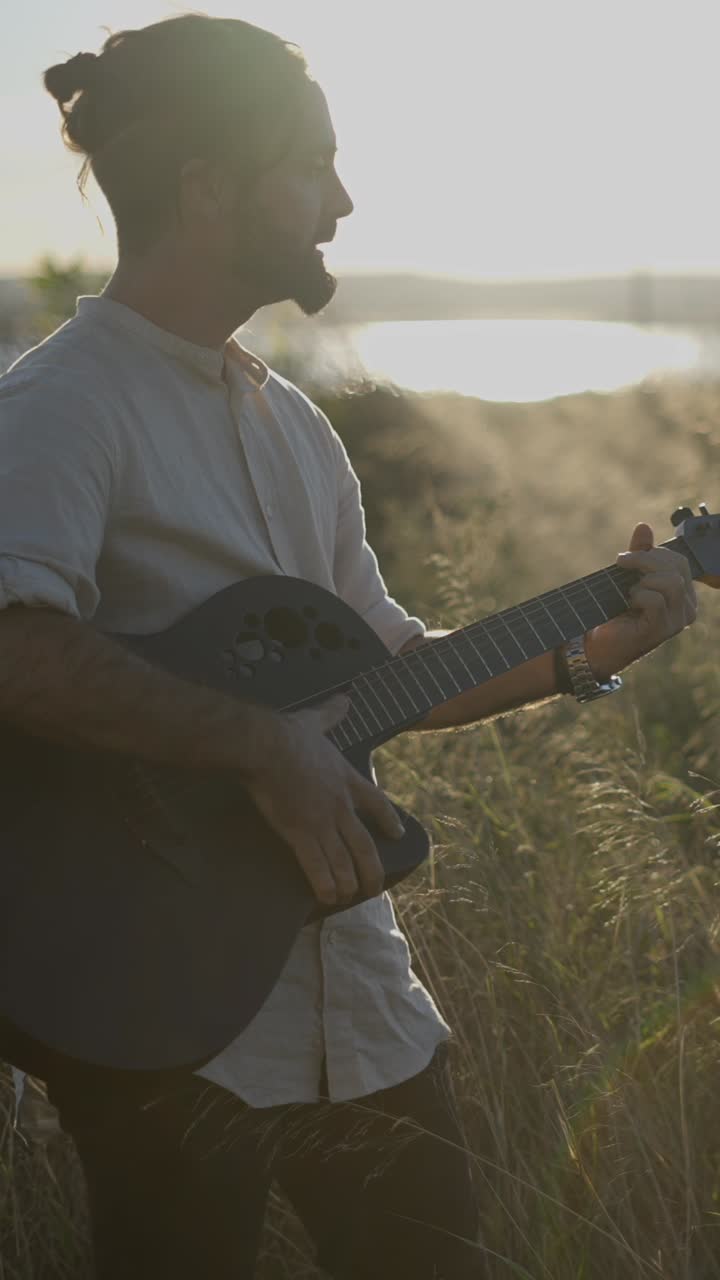 Man playing acoustic guitar in a field at sunset