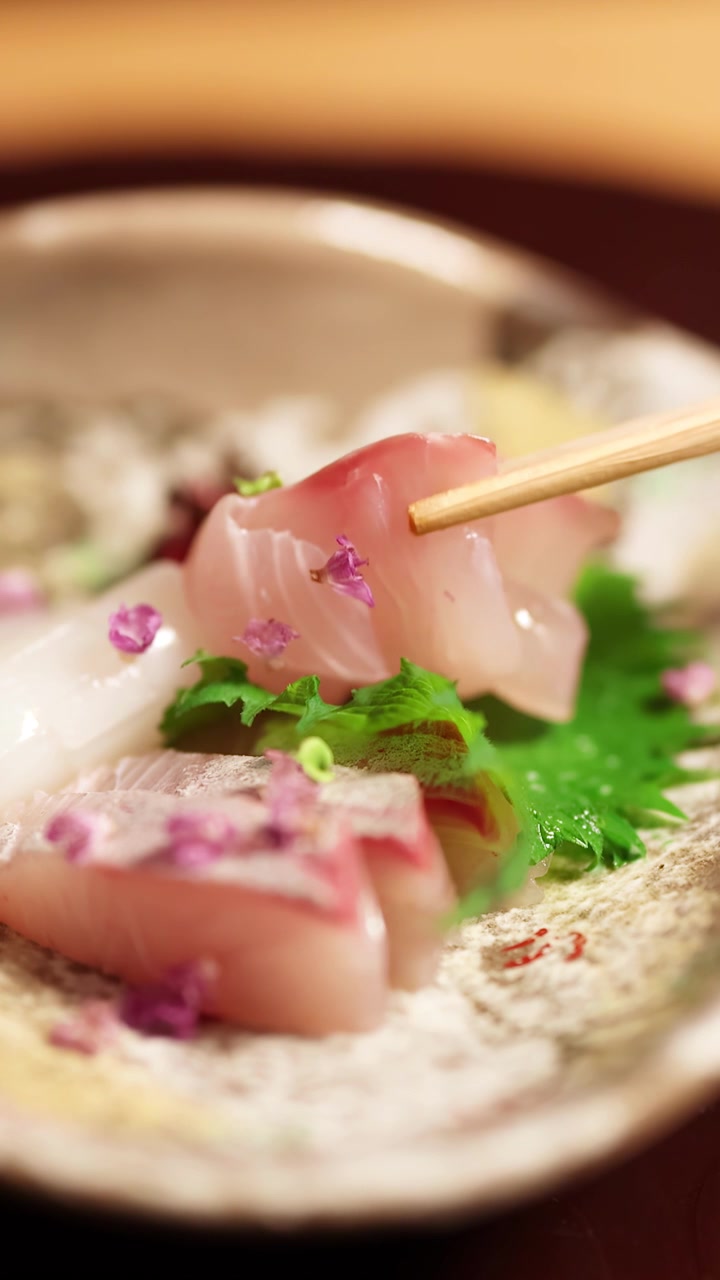 Primo piano di bacchette di legno che sollevano pesce crudo da un elegante piatto giapponese di frutti di mare.