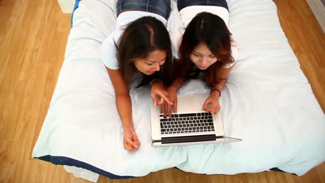 hermanas atractivas acostadas en la cama usando una computadora portátil