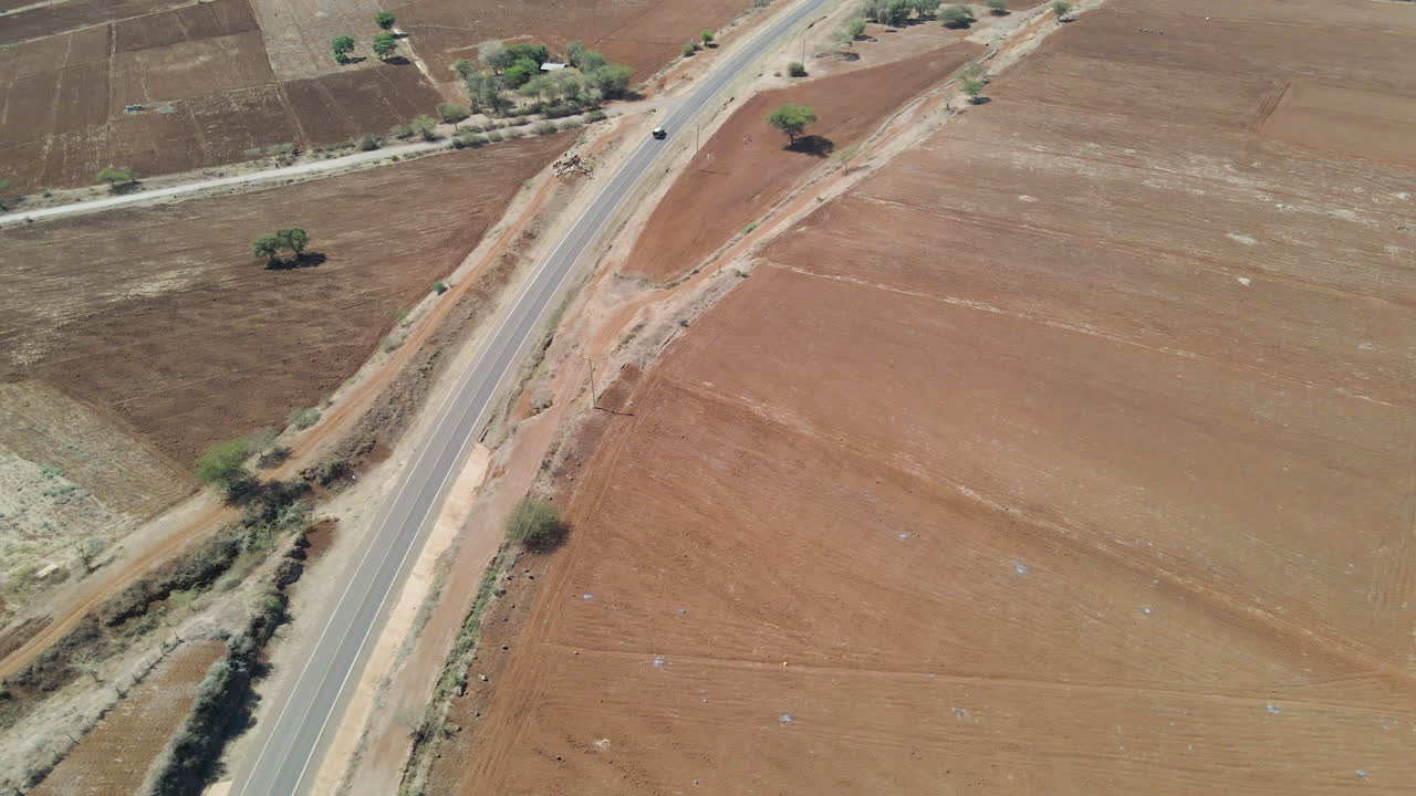 dolly aéreo de un automóvil que circula por una carretera solitaria a través de un paisaje seco en las zonas rurales de kenia