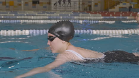 lateral tracking shot of a young female swimmer swimming breaststroke in indoor pool