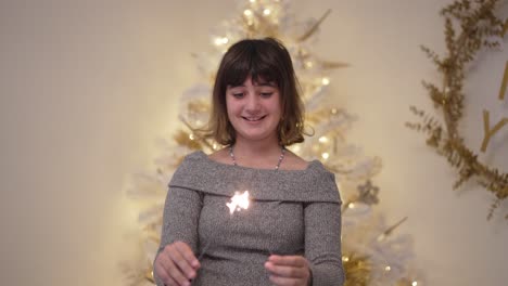 a girl lights christmas sparklers in slow motion with tree in background