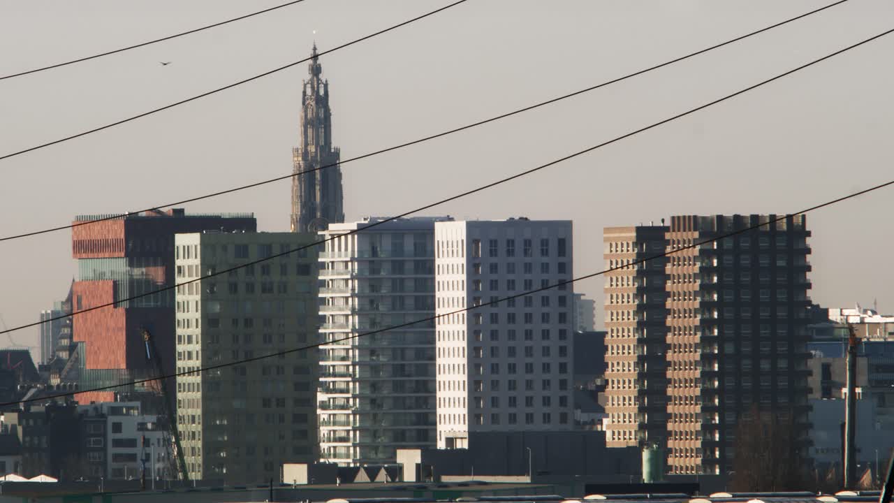 Cityscape of Antwerp showing modern towers, cathedral and heat haze at sunrise with visible power lines