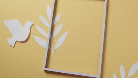 close up of white dove with frame and leaves and copy space on yellow background