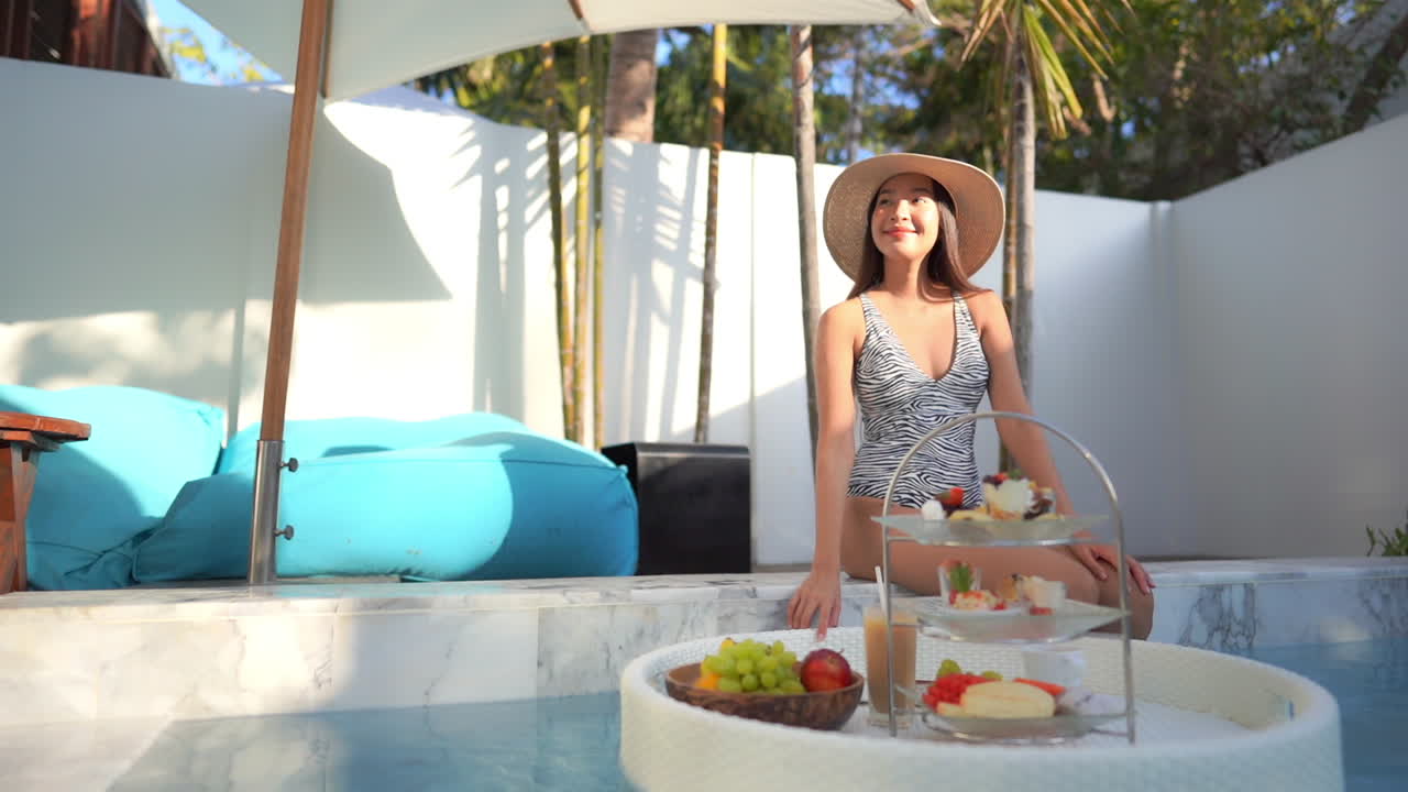 A young attractive woman sitting poolside steadies the floating banquet service platter of food with her hand