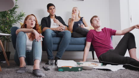 grupo de estudiantes universitarios en una casa compartida viendo televisión y comiendo pizza