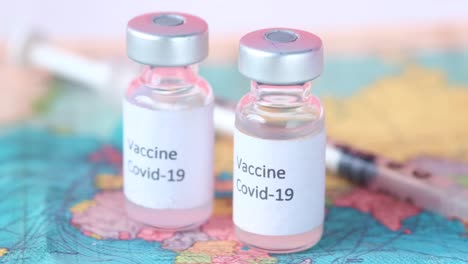 covid-19 vaccine vials and syringe on world map