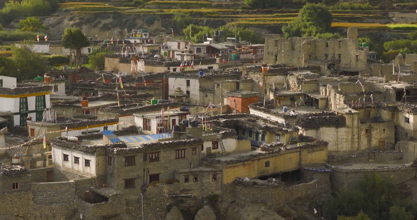 Kagbeni, Mustang, Nepal, toma de seguimiento lateral enfocándose en la arquitectura tradicional de adobe y casas históricas de piedra dañadas ubicadas bajo las colinas, rodeadas de tierras agrícolas