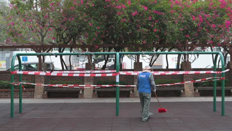 Ein-Stadtarbeiter-Fegt-Und-Reinigt-Einen-Geschlossenen-Spielplatz,-Während-Ein-Swing-spiel-Aufgrund-Des-Covid-19-coronavirus-ausbruchs-Und-Der-Einschränkungen-In-Hong-Kong-Vollständig-Aufgezeichnet-Wird