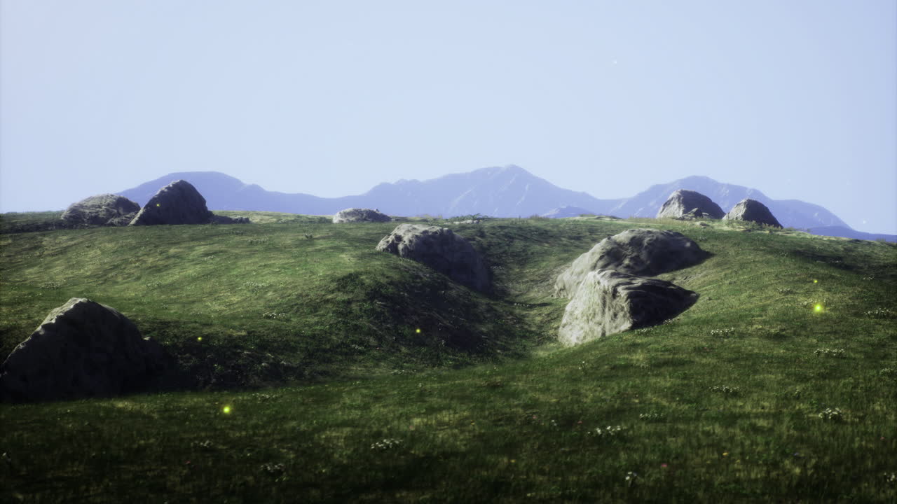 Rolling green hills with scattered rocks and distant mountains under clear sky