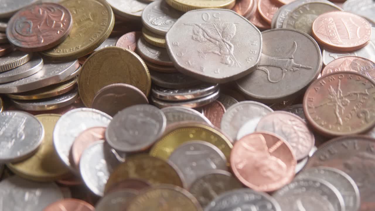 Assorted international coins from various countries and denominations, different sizes, values, colours. Slow camera movement past the coins, extreme close up