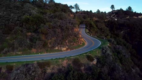 tight curve of mountain road beside steep cliff at dawn, drone orbit