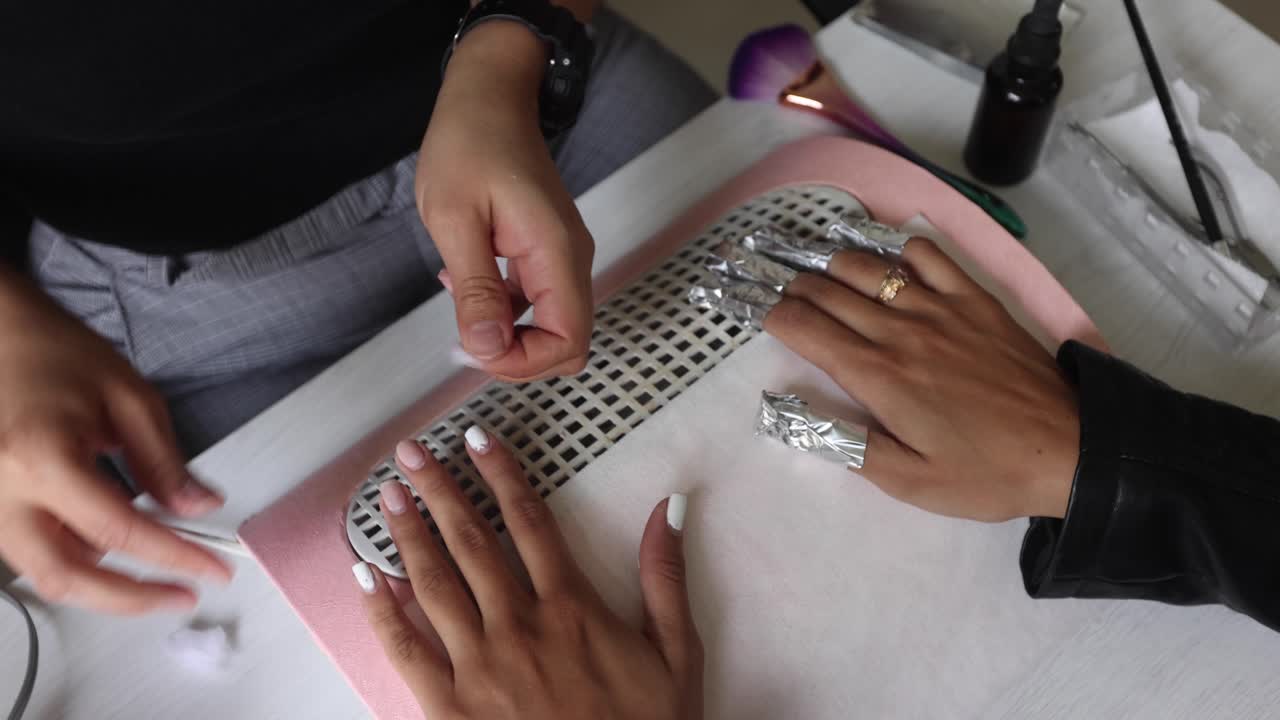 maestra usando papel de aluminio mientras hace manicura para el cliente en el salón