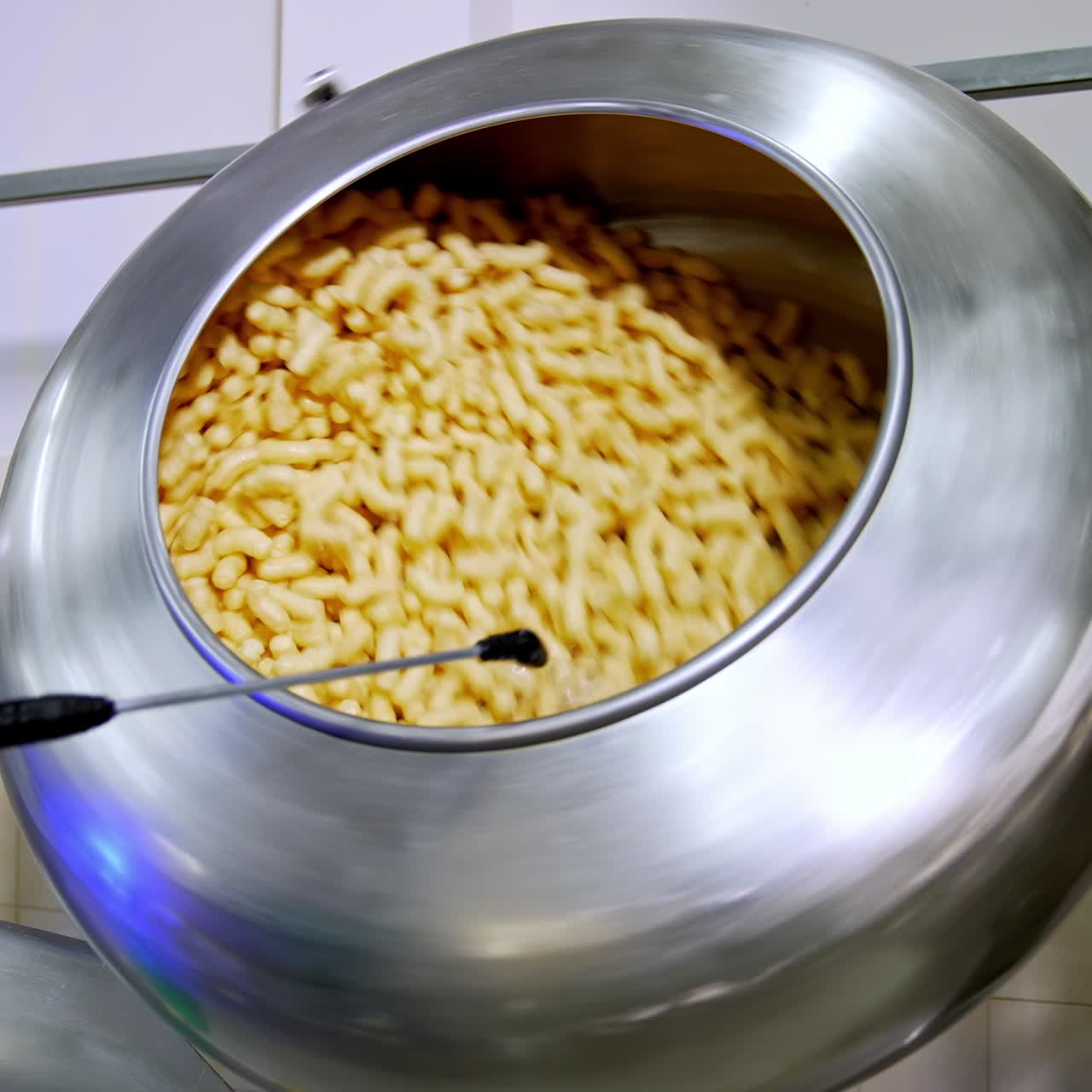 Corn snack sticks being sprayed with sweet syrup in the rotating tank. Snack production at modern food factory