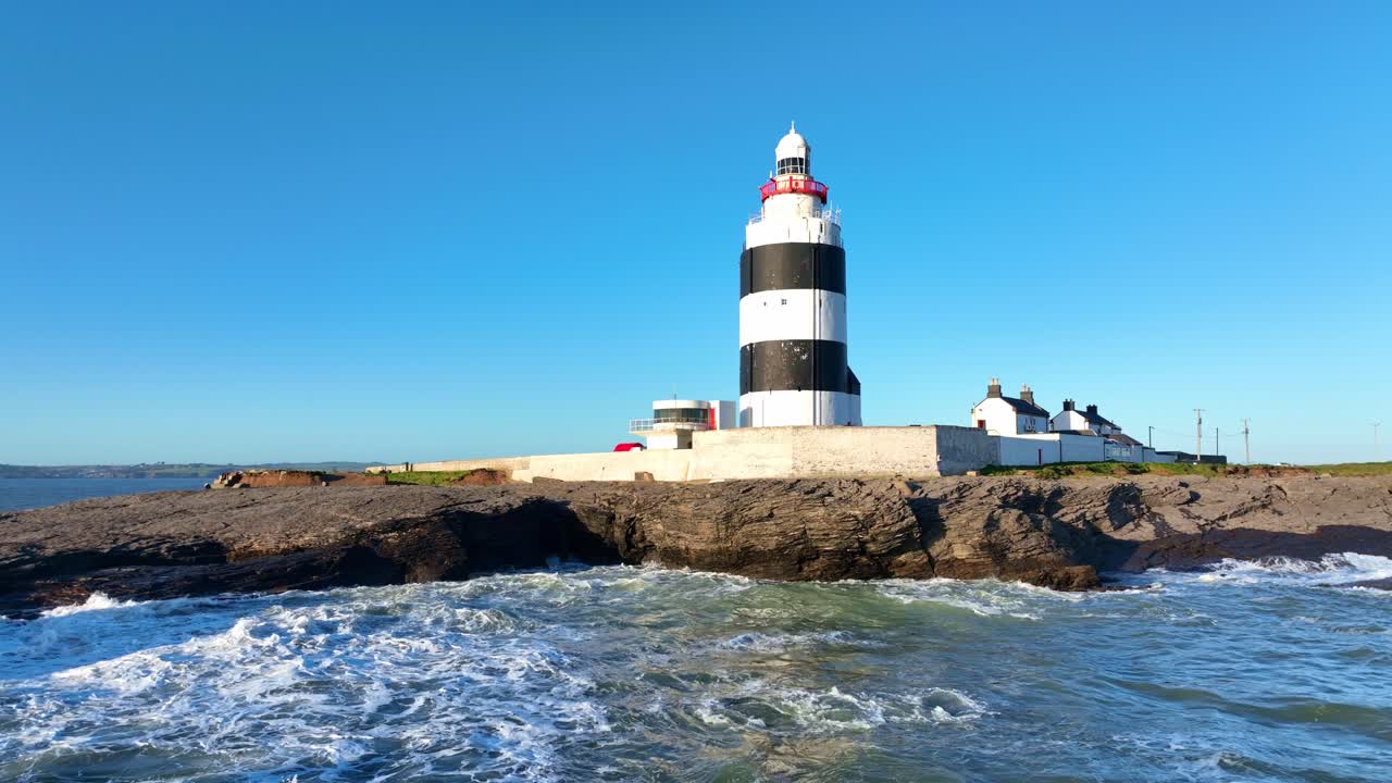 Faro di Hook Head, Wexford, Irlanda, ripresa drone in allontanamento a bassa quota sul mare con onde in arrivo in primavera