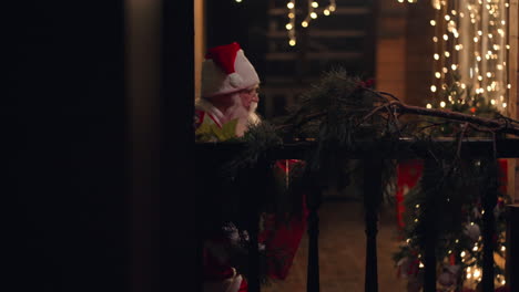 Side-view-Santa-Claus-is-carrying-a-gift-in-his-hands-in-winter-on-the-street-and-comes-to-the-door-and-enters-the-house-with-garlands-and-Christmas-decorations