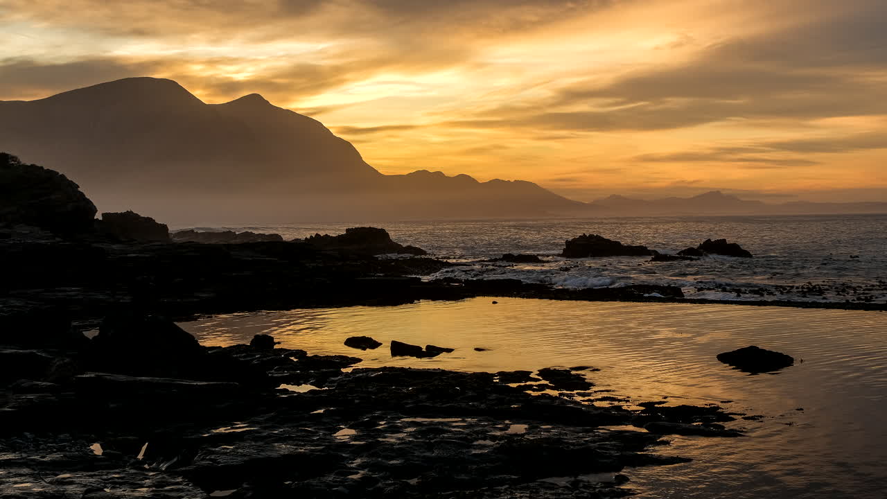 Motion time lapse of vibrant sunrise over Hermanus coastline and tide pool