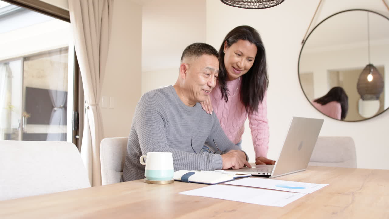 Senior asian couple smiling while using laptop at home, enjoying time together